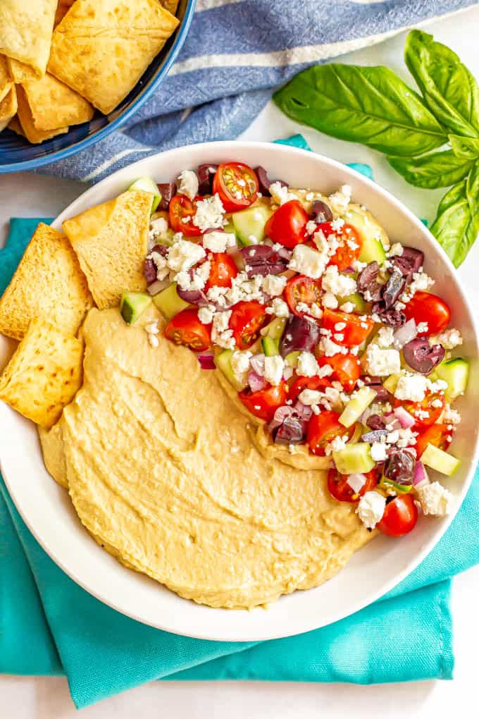 Hummus dip appetizer with chopped fresh veggies, feta cheese and pita chips for serving