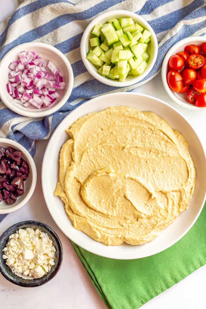 Ingredients for a layered hummus appetizer arranged in separate white bowls