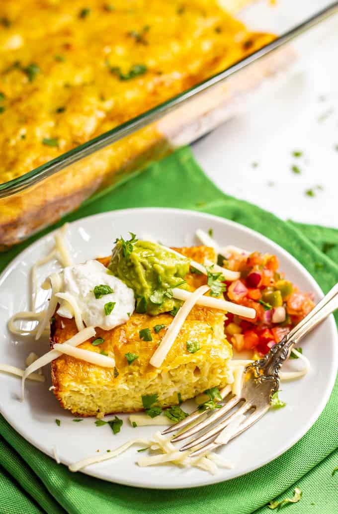 A slice of cheesy Mexican baked eggs served on a plate with toppings and a fork to the side