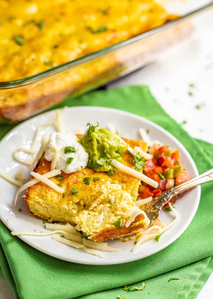 A slice of cheesy Mexican baked eggs served on a plate with toppings and a fork