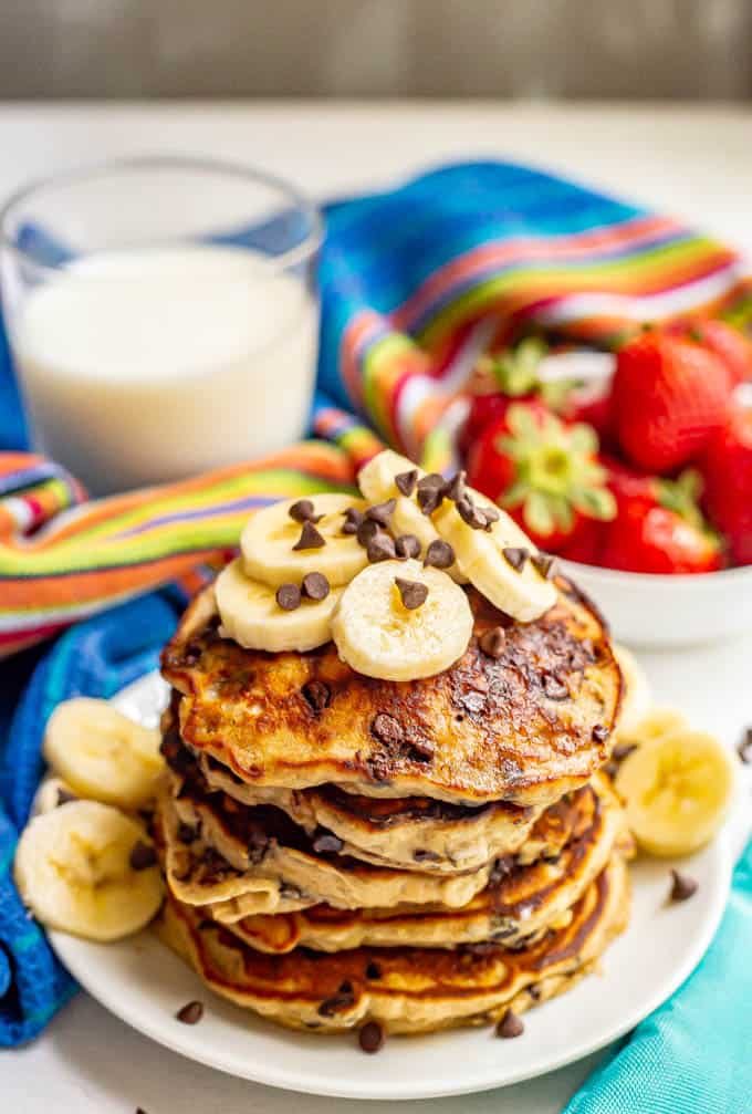 A stack of freshly made banana chocolate chip pancakes served with extra bananas and chocolate chips on top