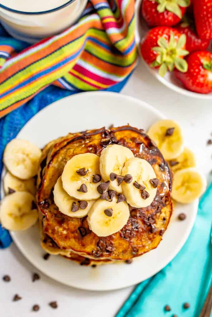 A stack of pancakes with chocolate chips and sliced bananas served on a white plate