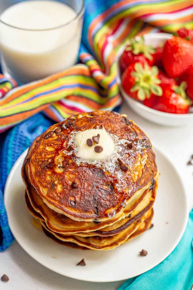 A stack of pancakes with chocolate chips and butter on a white plate