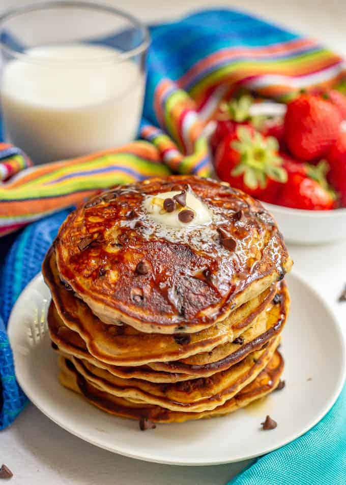 A big stack of chocolate chip pancakes with melted butter and maple syrup over top served on a white plate