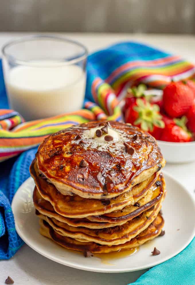 Stack of chocolate chip pancakes with butter and maple syrup served with milk and strawberries