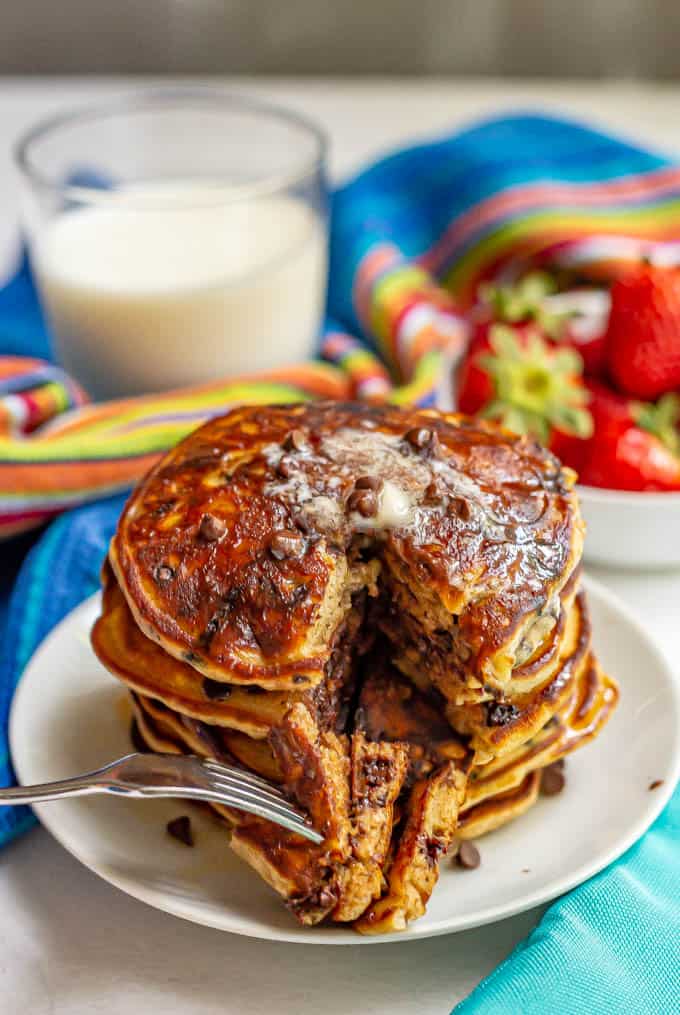 A fork piercing a bite of a stack of chocolate chip pancake son a plate with melted butter over the top.