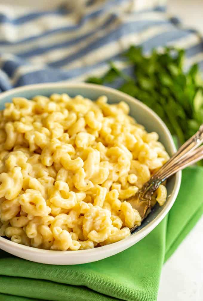 Easy macaroni and cheese pasta served in a bowl with green napkins underneath and parsley lying nearby