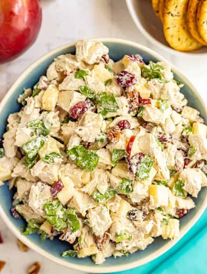 A serving bowl full of harvest chicken salad with apples, pecans, dried cranberries and spinach