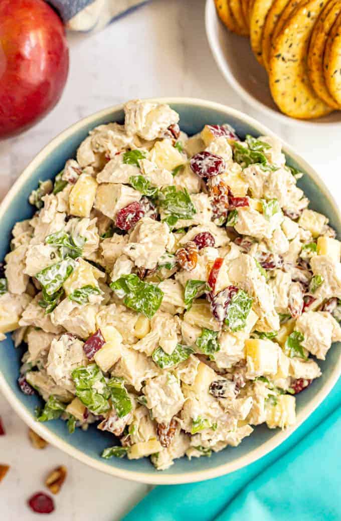 A serving bowl full of harvest chicken salad with apples, pecans, dried cranberries and spinach