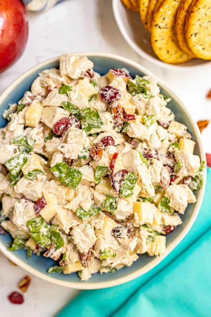 A serving bowl full of harvest chicken salad with apples, pecans, dried cranberries and spinach