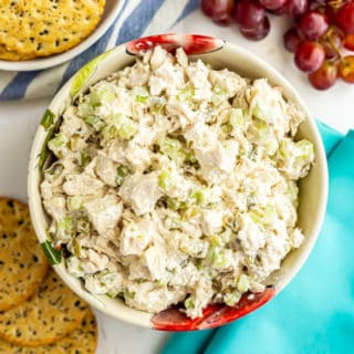 A bowl of classic chicken salad with crackers and grapes nearby