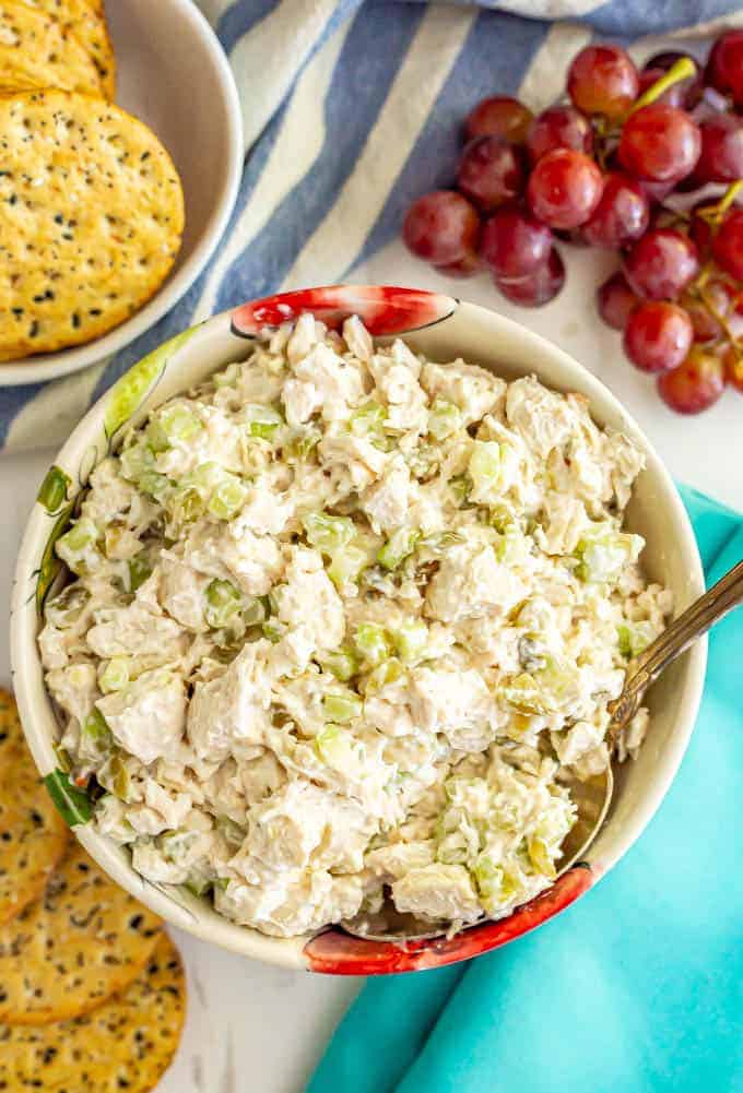 Classic chicken salad served in a bowl with a spoonful being taken and crackers and grapes