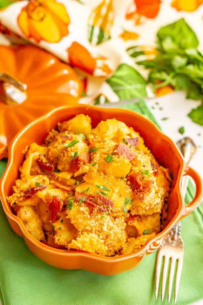 Creamy pumpkin mac and cheese with bacon in a pumpkin serving dish on a green napkin