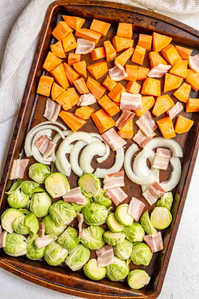 Sweet potatoes, onions, Brussels sprouts and bacon on a sheet pan before roasting