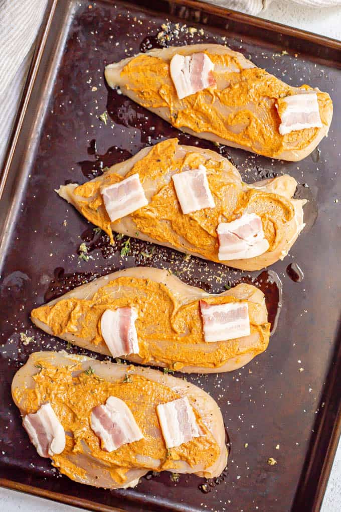 Chicken breasts with a mustard sauce and bacon on a sheet pan before cooking