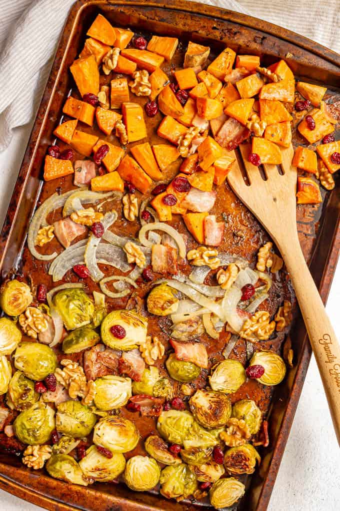 Mixed roasted vegetables on a sheet pan with a wooden spatula