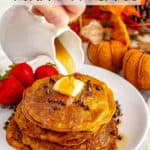 Whole wheat pumpkin pancakes stacked on a white plate with a pat of butter on top and maple syrup being poured over them.