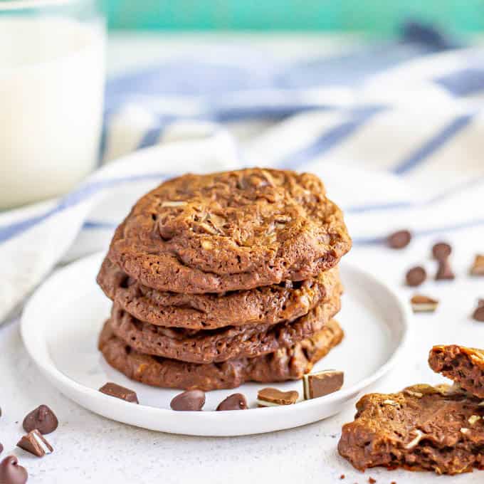 A stack of chocolate cookies on a white plate with a glass of milk