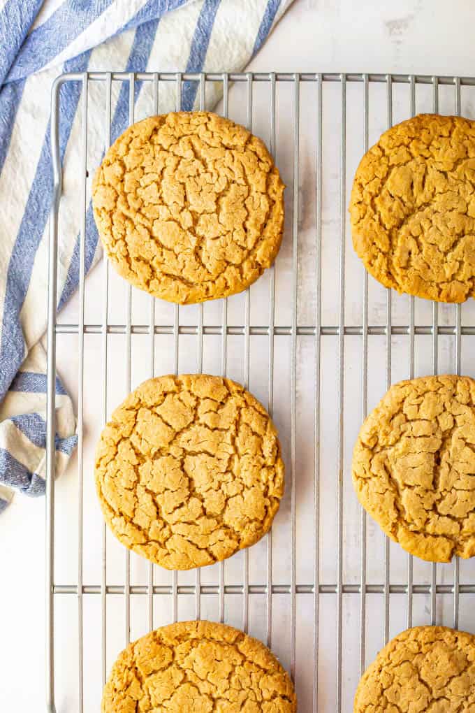 Large peanut butter cookies on a cooling rack with a blue striped towel nearby