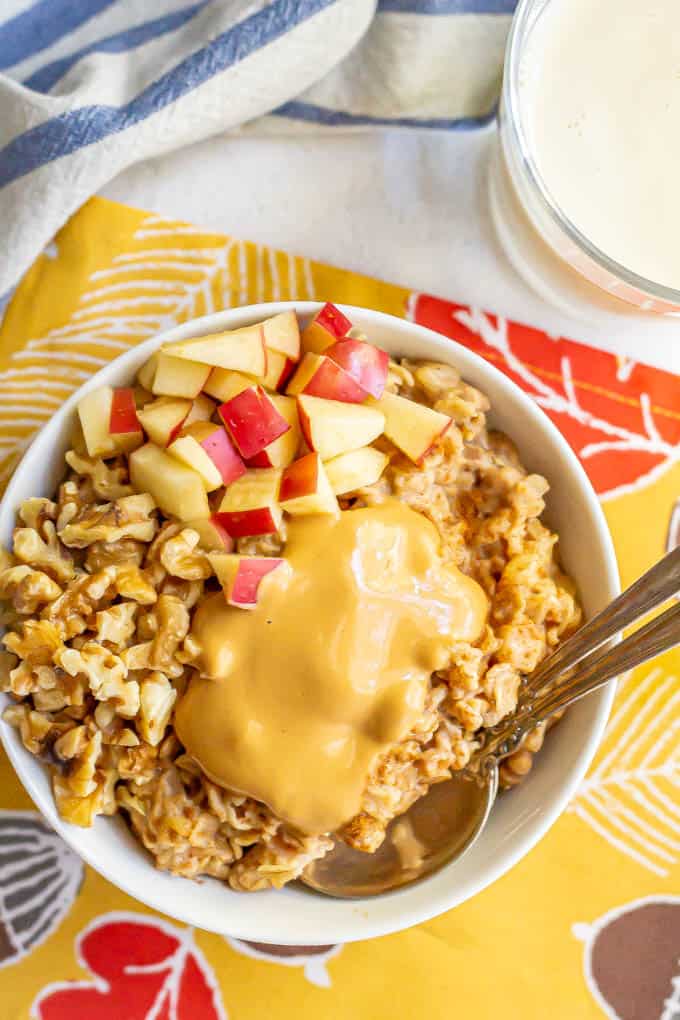 Peanut butter oatmeal with peanut butter, apples and walnuts on top and 2 spoons for eating