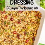 A wild rice dressing with mushrooms, celery and dried cranberries in a white baking dish with herbs for garnish.