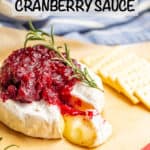 Melted baked brie on a piece of parchment paper with cranberry sauce and a sprig of rosemary on top, crackers to the side and a text overlay on the photo.
