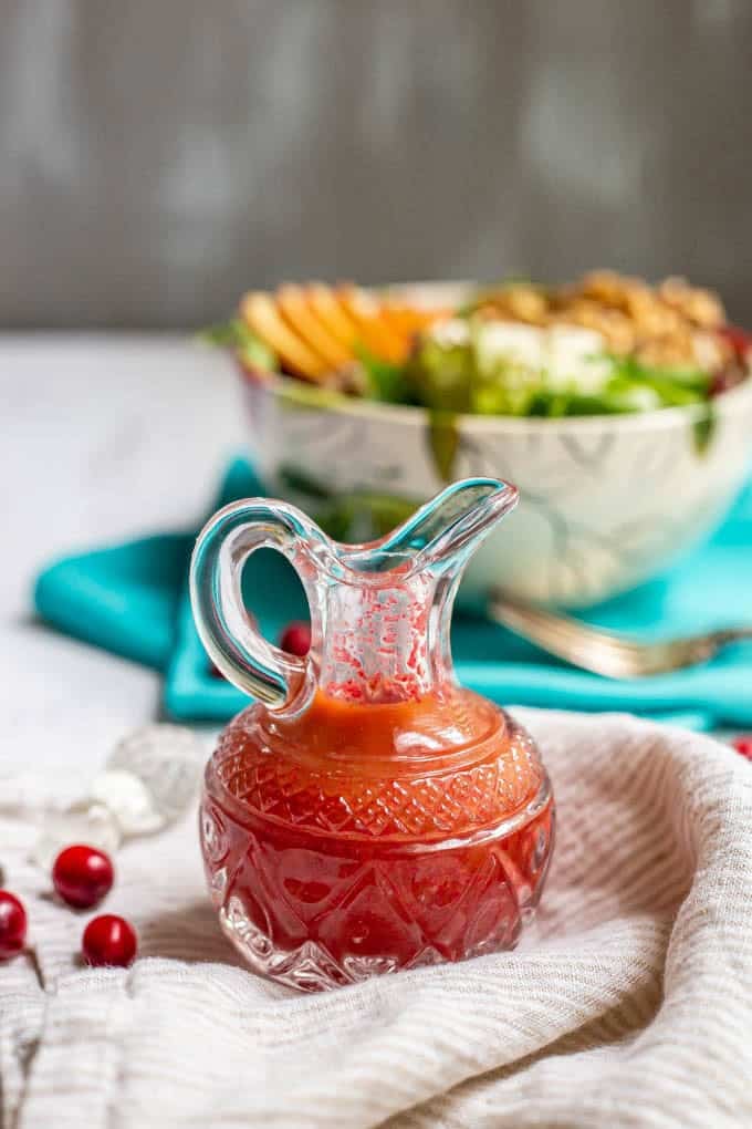 Cranberry vinaigrette dressing in a pouring glass with fresh cranberries nearby