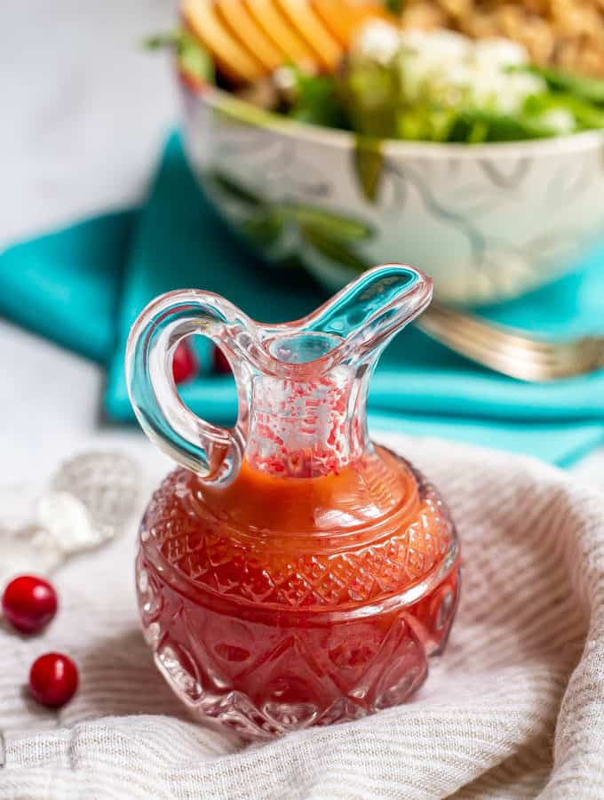 Fresh cranberry vinaigrette dressing in a pouring glass with fresh cranberries nearby