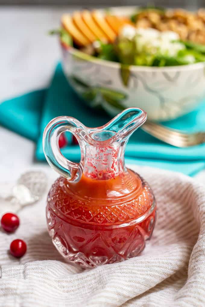 Fresh cranberry vinaigrette dressing in a pouring glass with fresh cranberries nearby