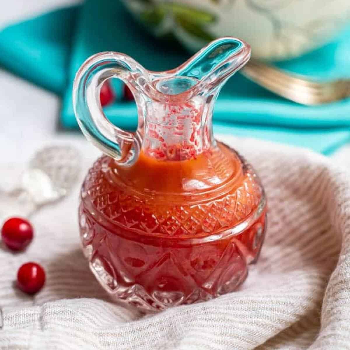 Fresh cranberry vinaigrette dressing in a pouring glass with fresh cranberries nearby