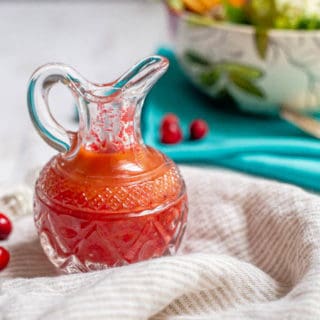 Cranberry salad dressing in a decorated glass server with fresh cranberries scattered around