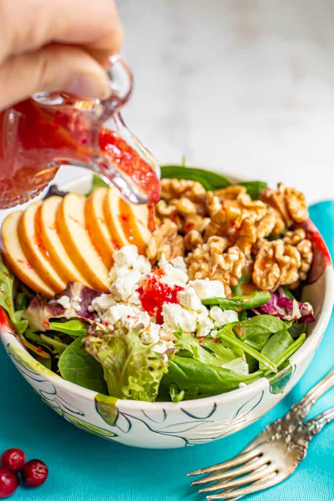 Cranberry vinaigrette being poured over a mixed green salad in a bowl