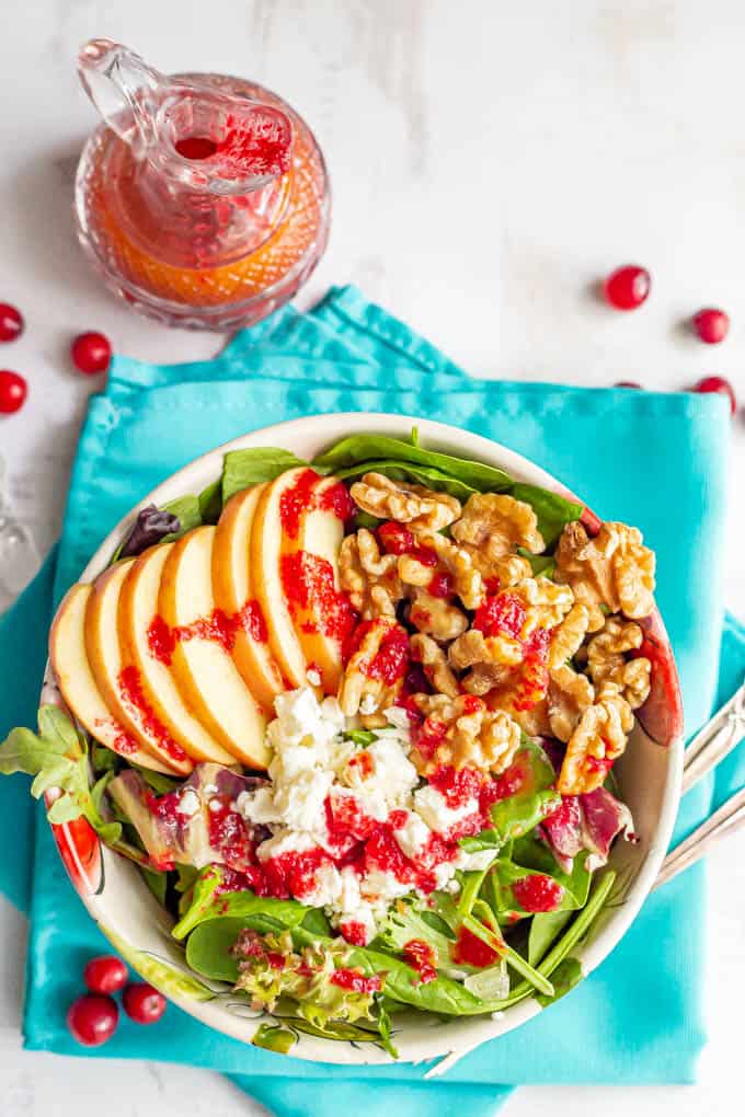 A salad bowl with greens, apples, walnuts and feta cheese and cranberry dressing drizzled over top