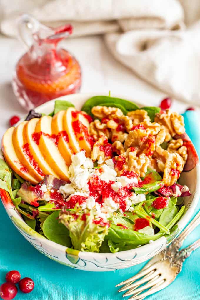 A salad bowl with greens, apples, walnuts and feta cheese and cranberry vinaigrette drizzled over top