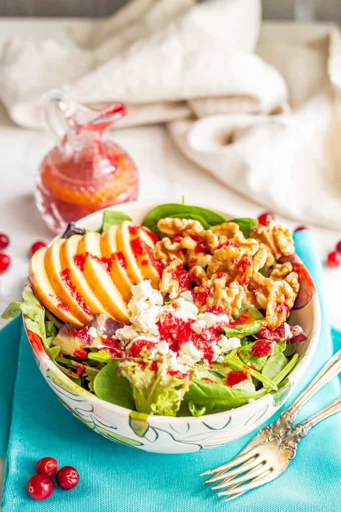 A salad bowl with greens, apples, walnuts and feta cheese and cranberry vinaigrette drizzled over top