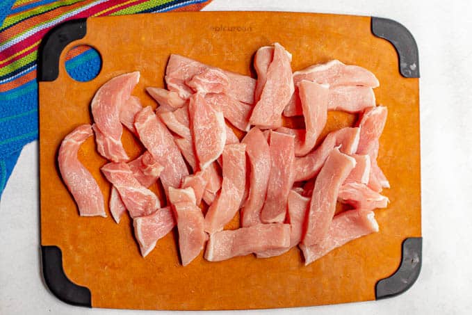 Thinly cut pork strips on a cutting board before being cooked