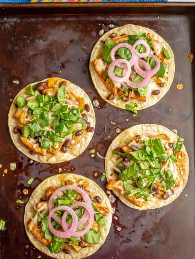 Four pork tostadas on a baking sheet with toppings added after being cooked