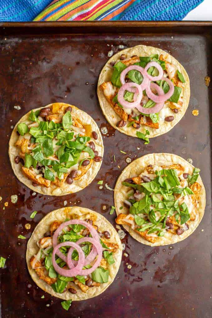 Four pork tostadas on a baking sheet with toppings added after being cooked