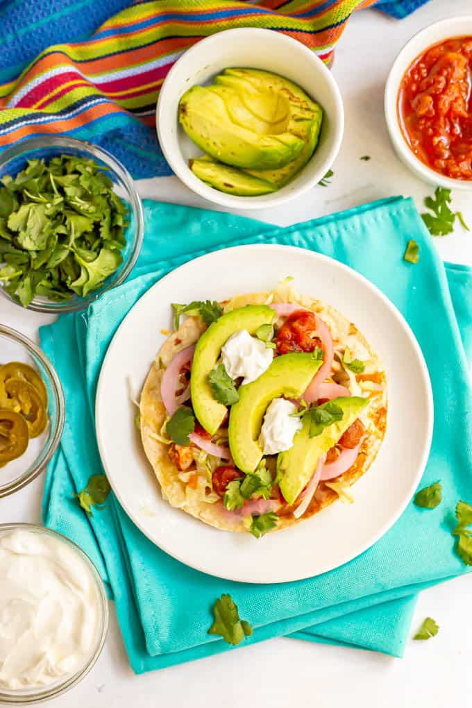 Turkey tostada served on a white plate with bowls of toppings nearby