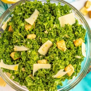Kale Caesar salad with croutons and shaved Parmesan in a large glass bowl with napkins and forks nearby
