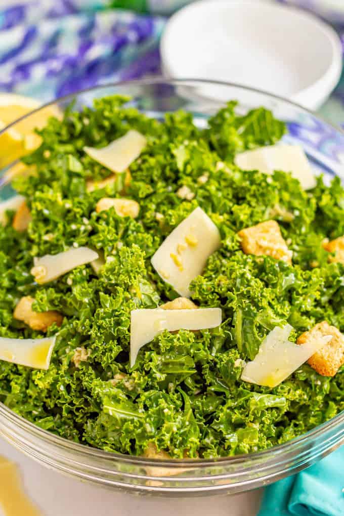 Kale Caesar salad with Parmesan and croutons in a large glass bowl with colorful napkins nearby