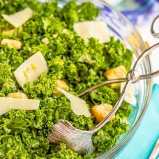 Salad tongs in a glass bowl with kale Caesar salad