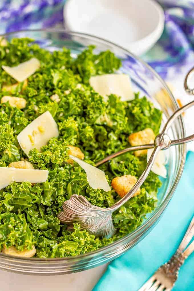 Salad tongs in a glass bowl with kale Caesar salad