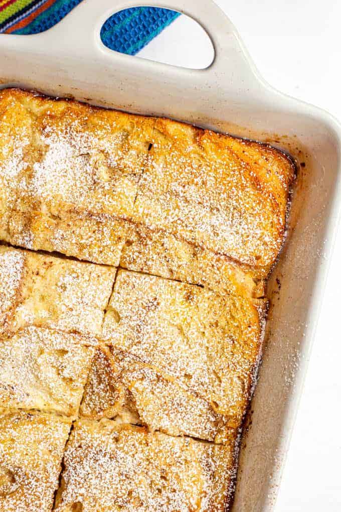 Baked French toast casserole in the white casserole dish with powdered sugar on top