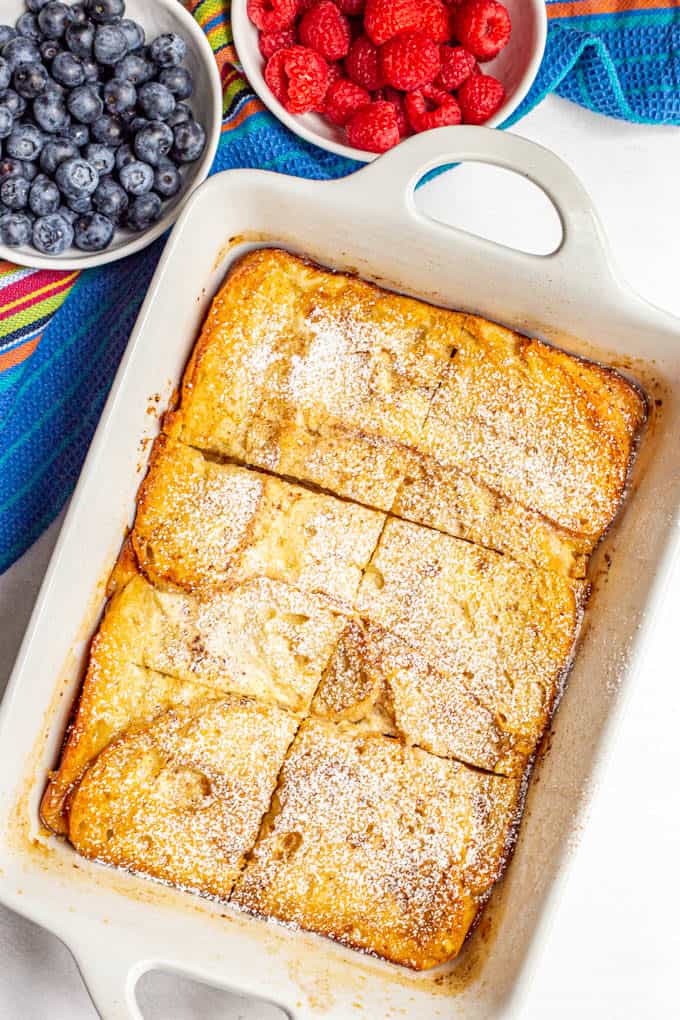 Baked French toast casserole in the white casserole dish with powdered sugar on top