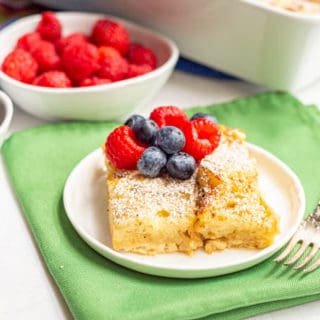 A slice of overnight French toast served on a white plate with fresh berries and a fork alongside
