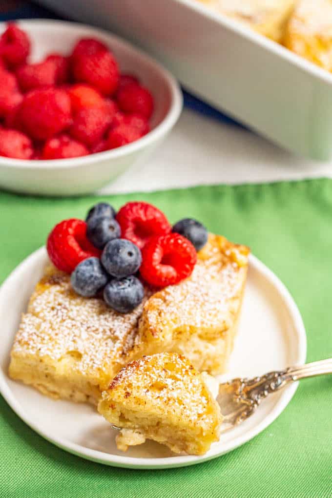 Baked French toast served on a white plate with fresh berries on top and a bite taken out with a fork