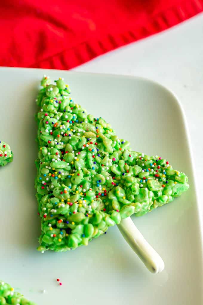 A green Rice Krispie Christmas tree with sprinkles on a white platter