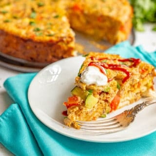 A slice of southwestern chicken and veggie frittata with sour cream and sriracha served on a white plate with a fork