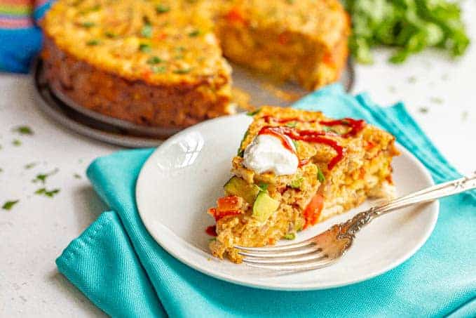 A slice of southwestern chicken and veggie frittata with sour cream and sriracha served on a white plate with a fork